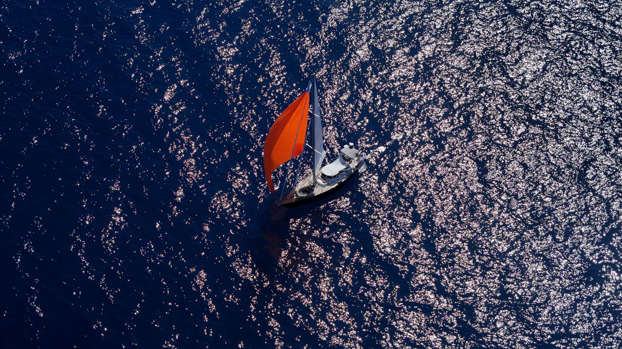 Luchtfoto van de Blue Beryl met oranje zeil op donkerblauwe zee
